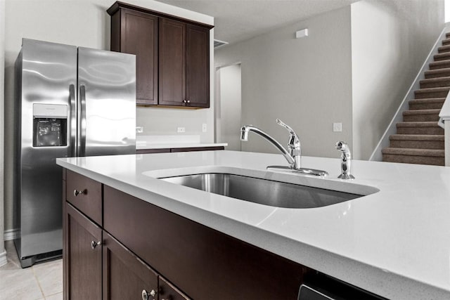 kitchen with sink, light tile patterned floors, dark brown cabinets, and stainless steel refrigerator with ice dispenser