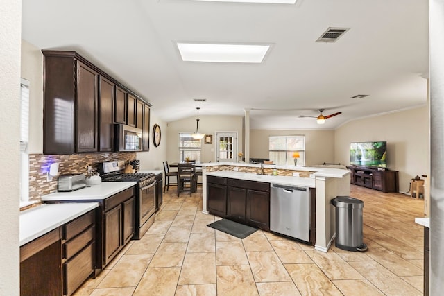 kitchen featuring appliances with stainless steel finishes, dark brown cabinets, an island with sink, decorative light fixtures, and vaulted ceiling