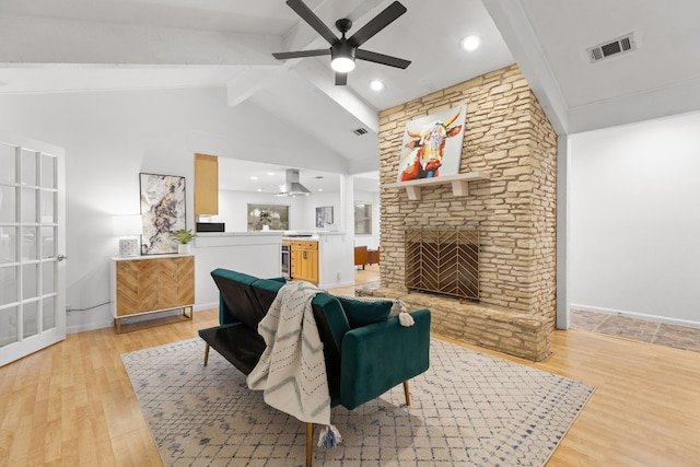 living room featuring a stone fireplace, high vaulted ceiling, light hardwood / wood-style flooring, beamed ceiling, and ceiling fan