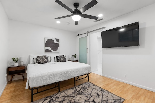 bedroom featuring hardwood / wood-style flooring, ceiling fan, and a barn door