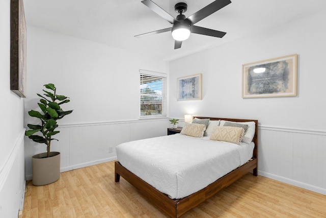 bedroom featuring a wainscoted wall, light wood-style flooring, and a ceiling fan