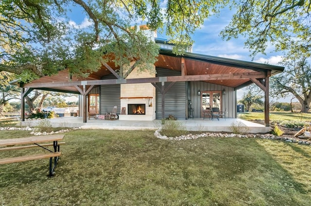 back of house with an outdoor fireplace, a yard, and a patio