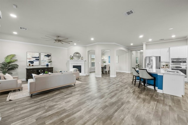 living room featuring ceiling fan, ornamental molding, and light hardwood / wood-style flooring