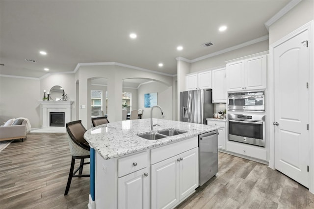 kitchen with sink, a breakfast bar area, stainless steel appliances, white cabinets, and a center island with sink