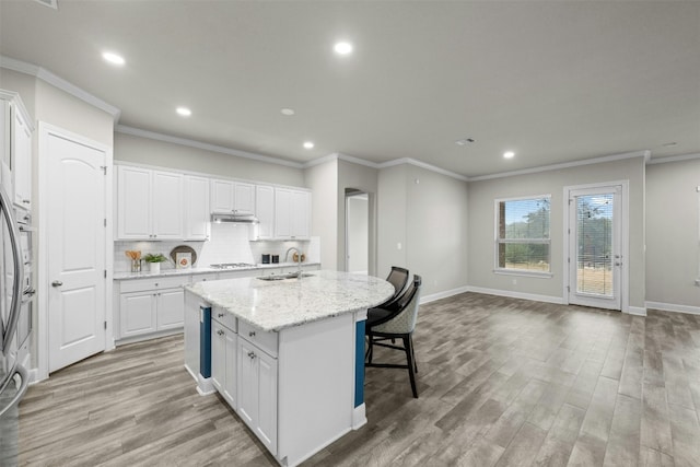 kitchen featuring stainless steel gas stovetop, sink, white cabinets, light stone counters, and a center island with sink