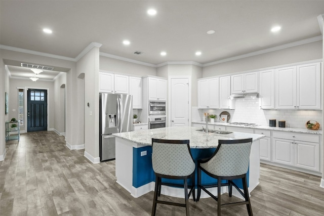 kitchen with white cabinetry, appliances with stainless steel finishes, a kitchen island with sink, and light stone counters