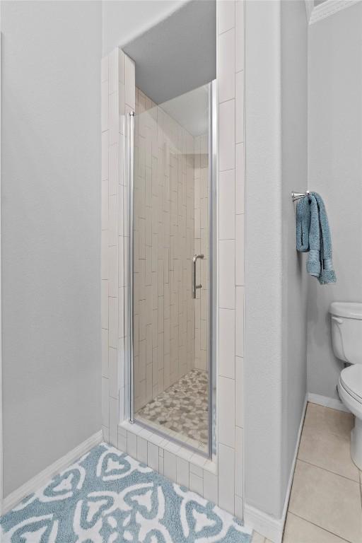 bathroom with tile patterned floors, toilet, and a shower with door