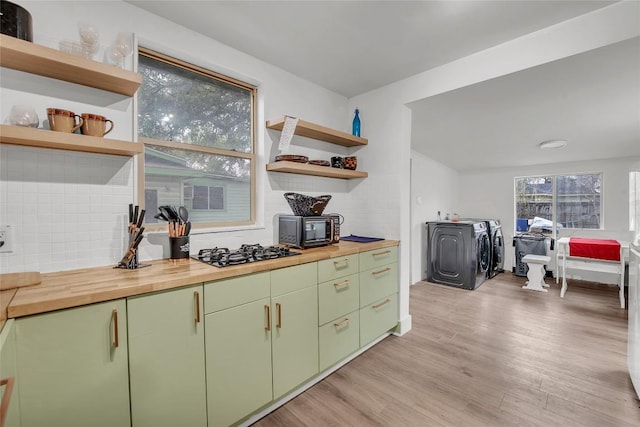 kitchen with stainless steel gas cooktop, wooden counters, light wood-type flooring, independent washer and dryer, and backsplash