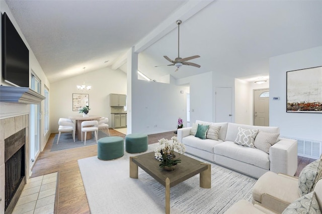 living room with high vaulted ceiling, a tiled fireplace, ceiling fan with notable chandelier, beamed ceiling, and light wood-type flooring