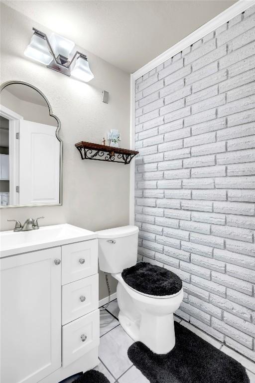 bathroom featuring tile patterned flooring, vanity, brick wall, and toilet