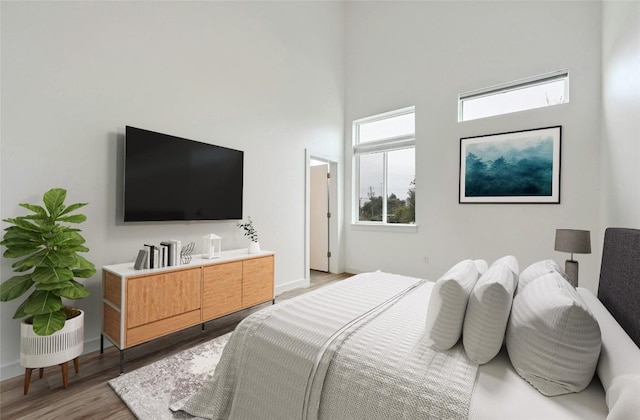 bedroom featuring baseboards, light wood-type flooring, and a towering ceiling