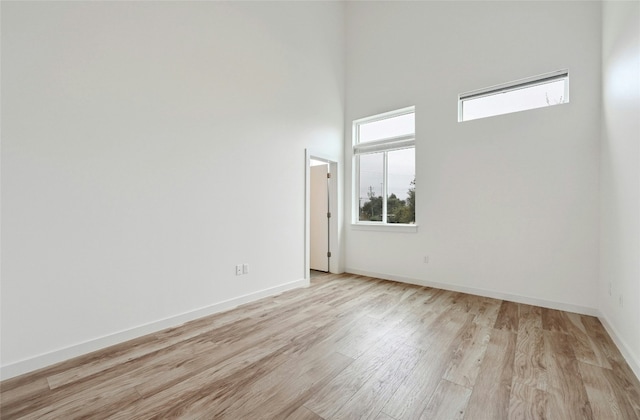 unfurnished room with a high ceiling, light wood-style flooring, and baseboards