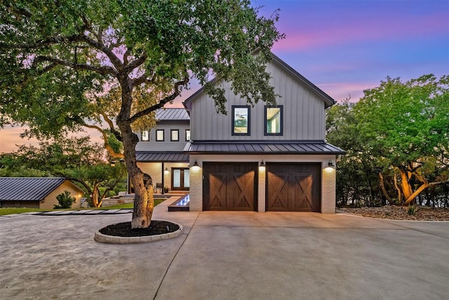 modern farmhouse style home featuring brick siding, an attached garage, a standing seam roof, metal roof, and driveway