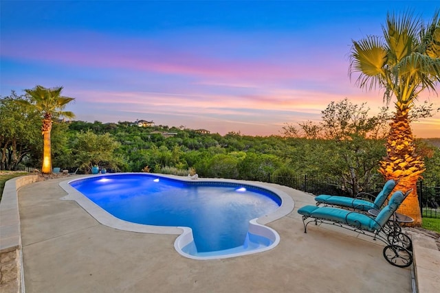 pool at dusk featuring fence, an outdoor pool, and a patio