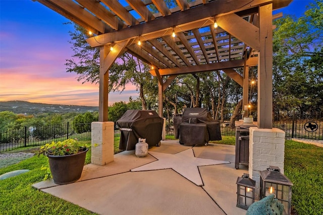 patio terrace at dusk with fence, grilling area, and a pergola