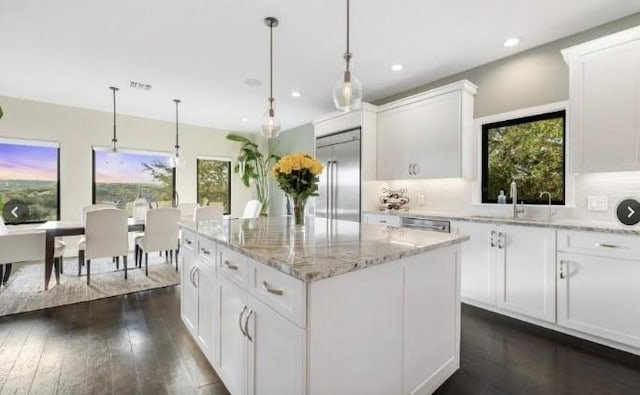 kitchen featuring dark wood finished floors, stainless steel appliances, decorative backsplash, a sink, and a kitchen island