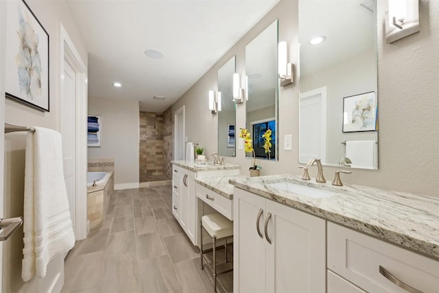 full bathroom featuring a garden tub, a shower stall, two vanities, and a sink