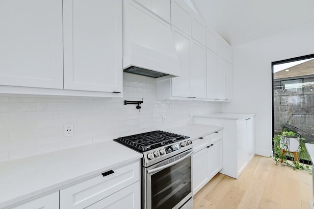 kitchen with tasteful backsplash, white cabinetry, gas range, custom range hood, and light hardwood / wood-style flooring