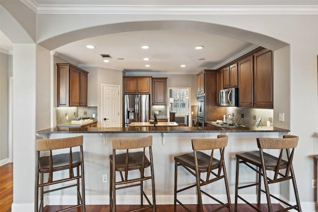 kitchen with stainless steel appliances, dark wood-type flooring, dark stone countertops, and a peninsula