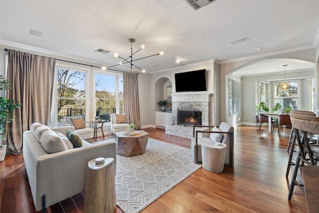 living room with a lit fireplace, crown molding, visible vents, and wood finished floors