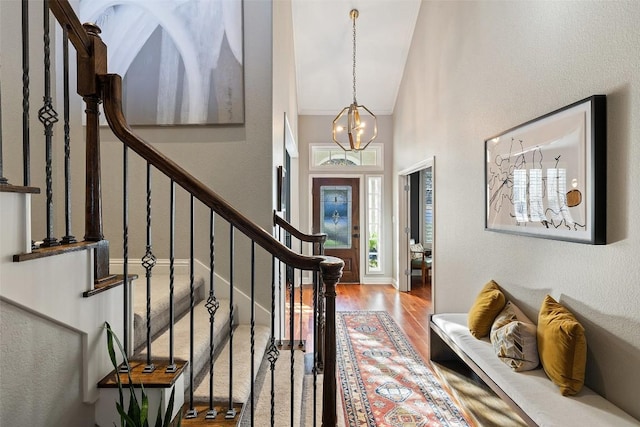 entrance foyer with high vaulted ceiling, stairway, wood finished floors, and an inviting chandelier