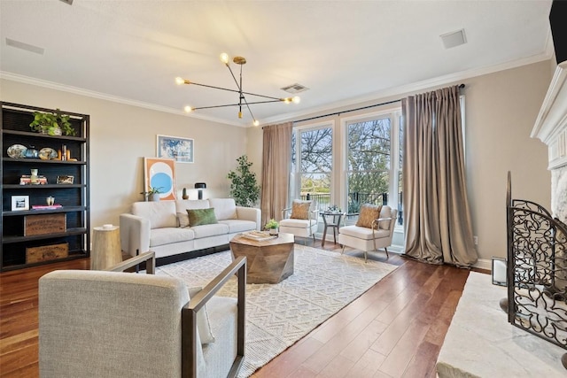 living area with ornamental molding, visible vents, a notable chandelier, and wood finished floors