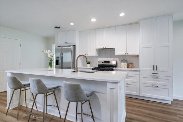 kitchen with an island with sink, appliances with stainless steel finishes, sink, and white cabinets