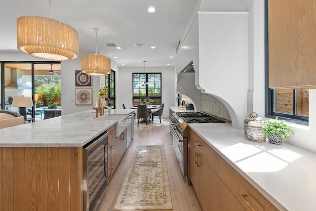 kitchen featuring decorative light fixtures, sink, beverage cooler, high end stainless steel range oven, and a spacious island