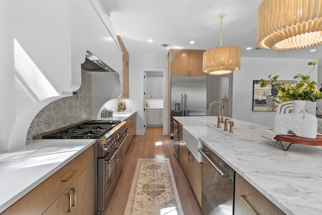 kitchen featuring high end appliances, tasteful backsplash, hanging light fixtures, light stone countertops, and light hardwood / wood-style floors