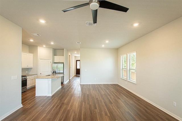 kitchen featuring dark wood-type flooring, light stone counters, appliances with stainless steel finishes, a kitchen island with sink, and white cabinets