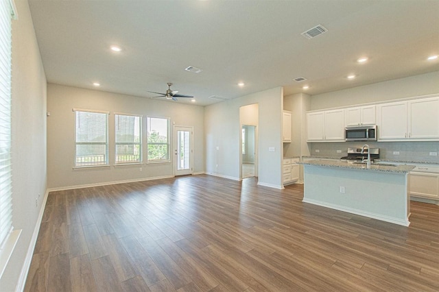 kitchen with white cabinetry, dark hardwood / wood-style floors, light stone countertops, and an island with sink