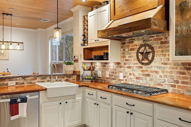 kitchen with wood counters, hanging light fixtures, appliances with stainless steel finishes, custom range hood, and white cabinets