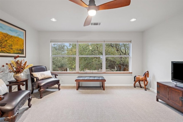 living area with plenty of natural light, light carpet, and ceiling fan