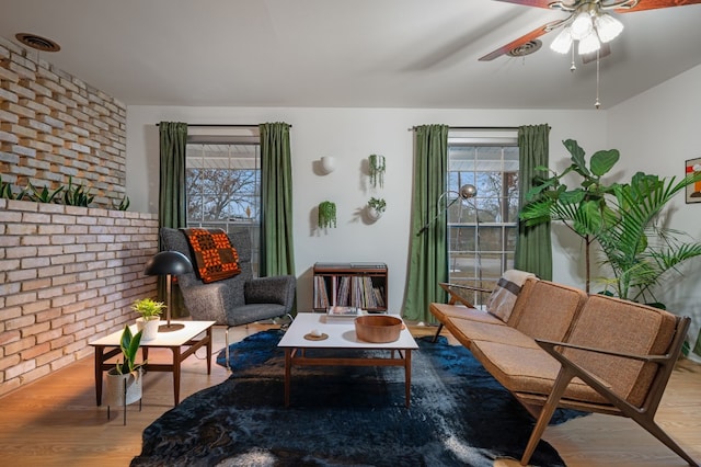 sitting room with light hardwood / wood-style floors, ceiling fan, and brick wall