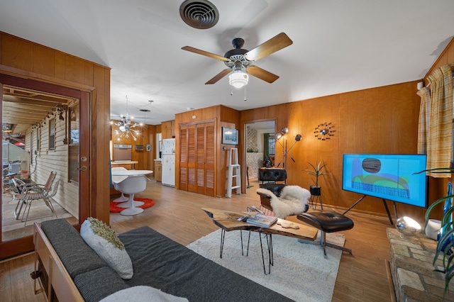 living room featuring ceiling fan with notable chandelier, light hardwood / wood-style flooring, and wood walls