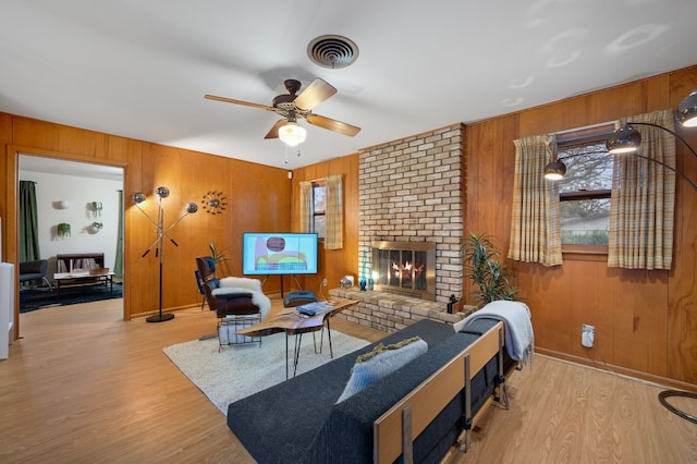 living room with a brick fireplace, wood walls, and light hardwood / wood-style flooring