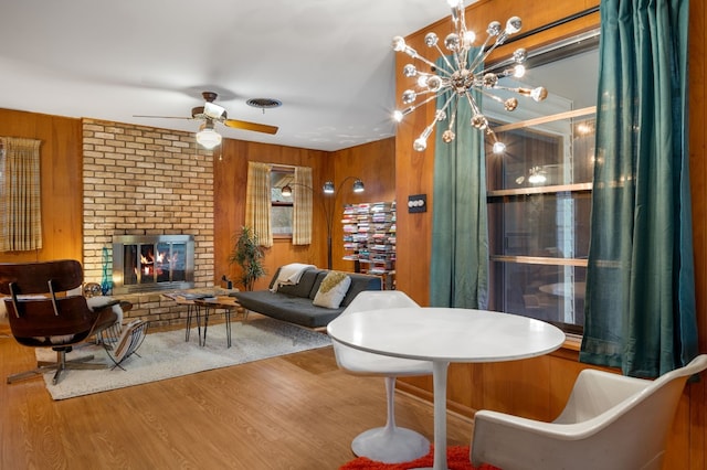 living room featuring a brick fireplace, wooden walls, wood-type flooring, and ceiling fan