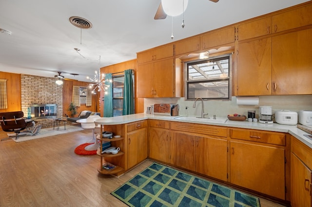 kitchen featuring sink, light hardwood / wood-style flooring, a fireplace, ceiling fan with notable chandelier, and kitchen peninsula