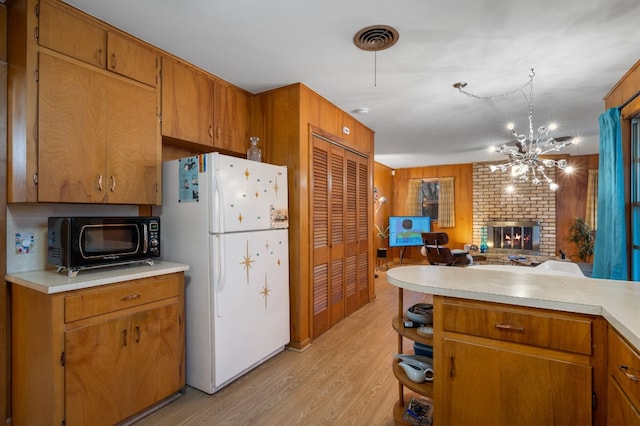 kitchen with light hardwood / wood-style flooring, wooden walls, white refrigerator, a fireplace, and decorative light fixtures