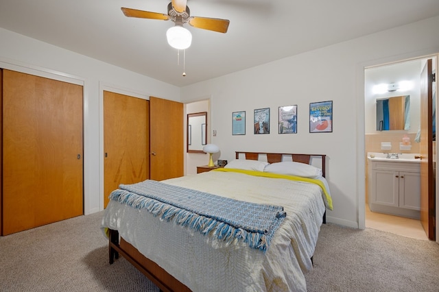 bedroom with sink, ensuite bath, light colored carpet, two closets, and ceiling fan