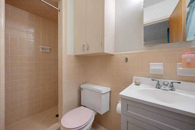 bathroom with a tile shower, vanity, tile walls, and toilet