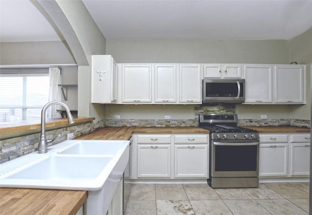 kitchen with wood counters, sink, light tile patterned floors, stainless steel appliances, and white cabinets