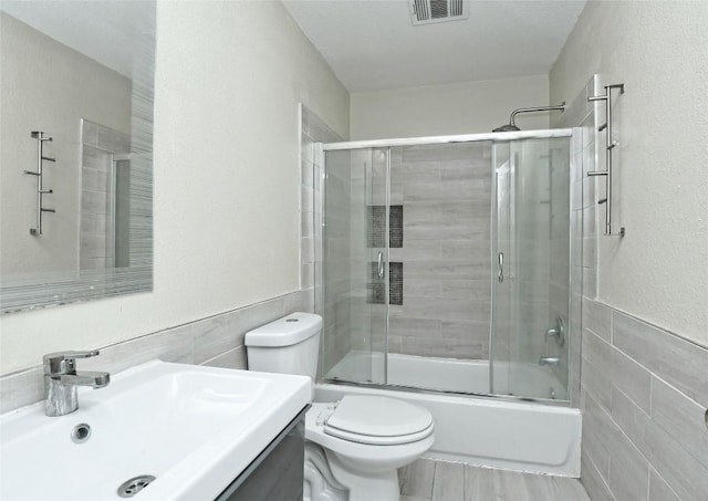 full bathroom featuring tile walls, vanity, shower / bath combination with glass door, and toilet