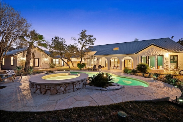 back house at dusk featuring a swimming pool with hot tub and a patio area