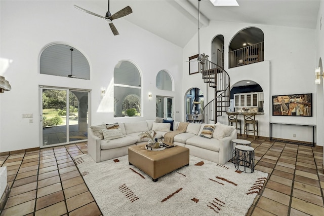 living room with a skylight, high vaulted ceiling, ceiling fan, beam ceiling, and tile patterned flooring