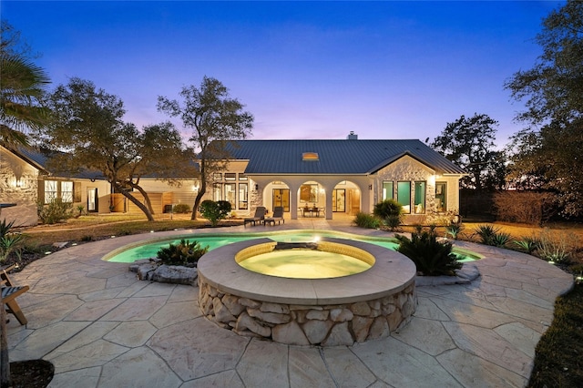 back house at dusk with a swimming pool with hot tub and a patio