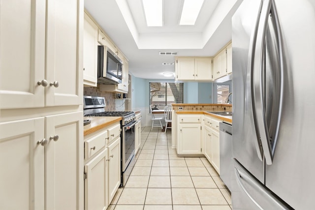 kitchen with sink, stainless steel appliances, light tile patterned flooring, decorative backsplash, and a raised ceiling