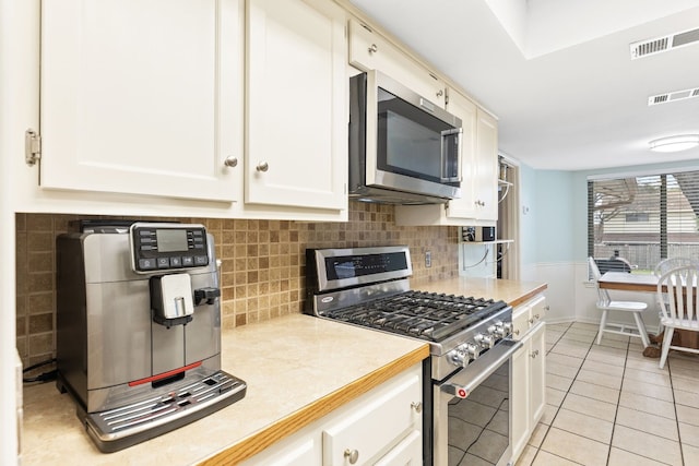 kitchen featuring white cabinetry, stainless steel appliances, decorative backsplash, and light tile patterned floors