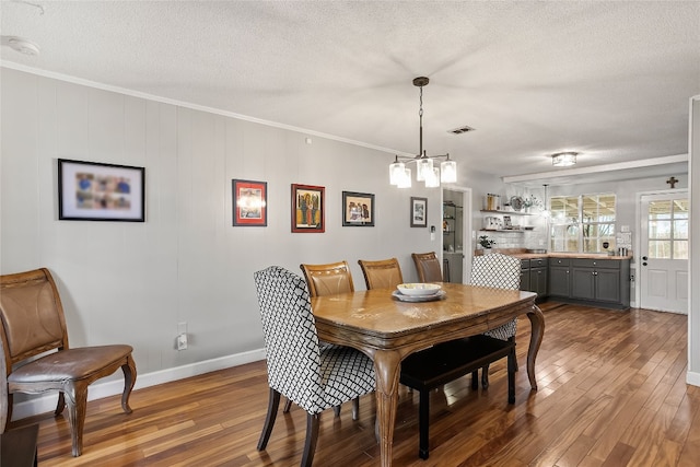 dining room featuring dark wood-type flooring, ornamental molding, an inviting chandelier, and a textured ceiling