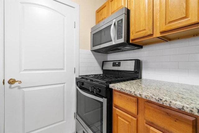 kitchen with stainless steel appliances, light stone counters, and decorative backsplash